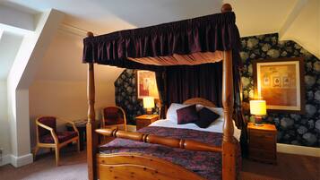 A four-poster bed with a canopy, a wooden nightstand with a lamp, a chair, and a framed picture on the wall.