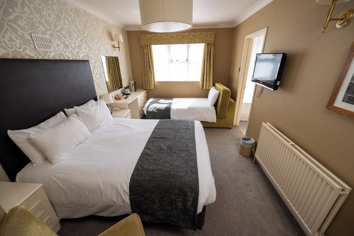 A hotel room with a large bed, a smaller bed, a desk, a chair, a TV, and a window with curtains.
