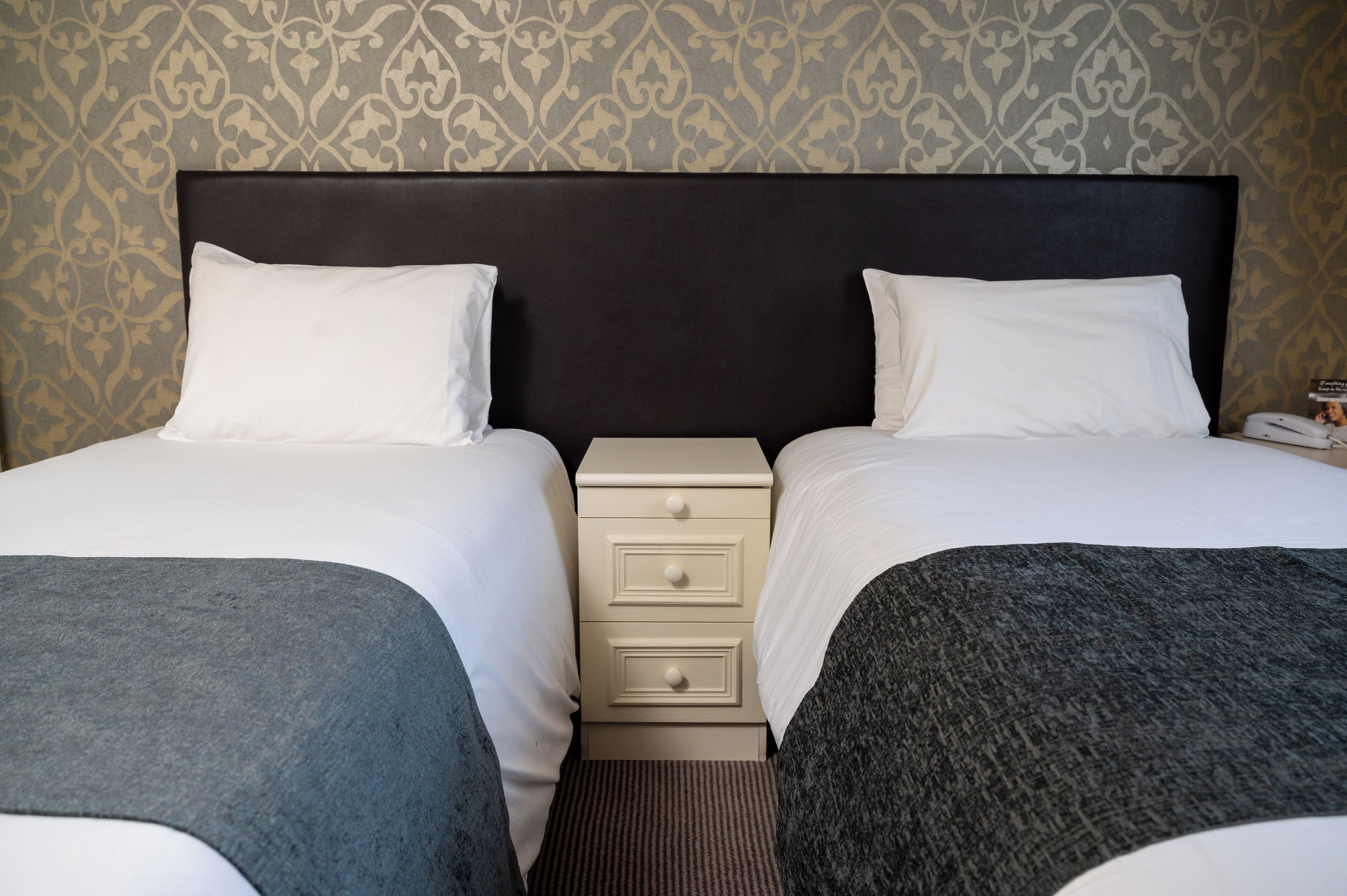 A hotel room with two beds, a nightstand, and a patterned wallpaper.
