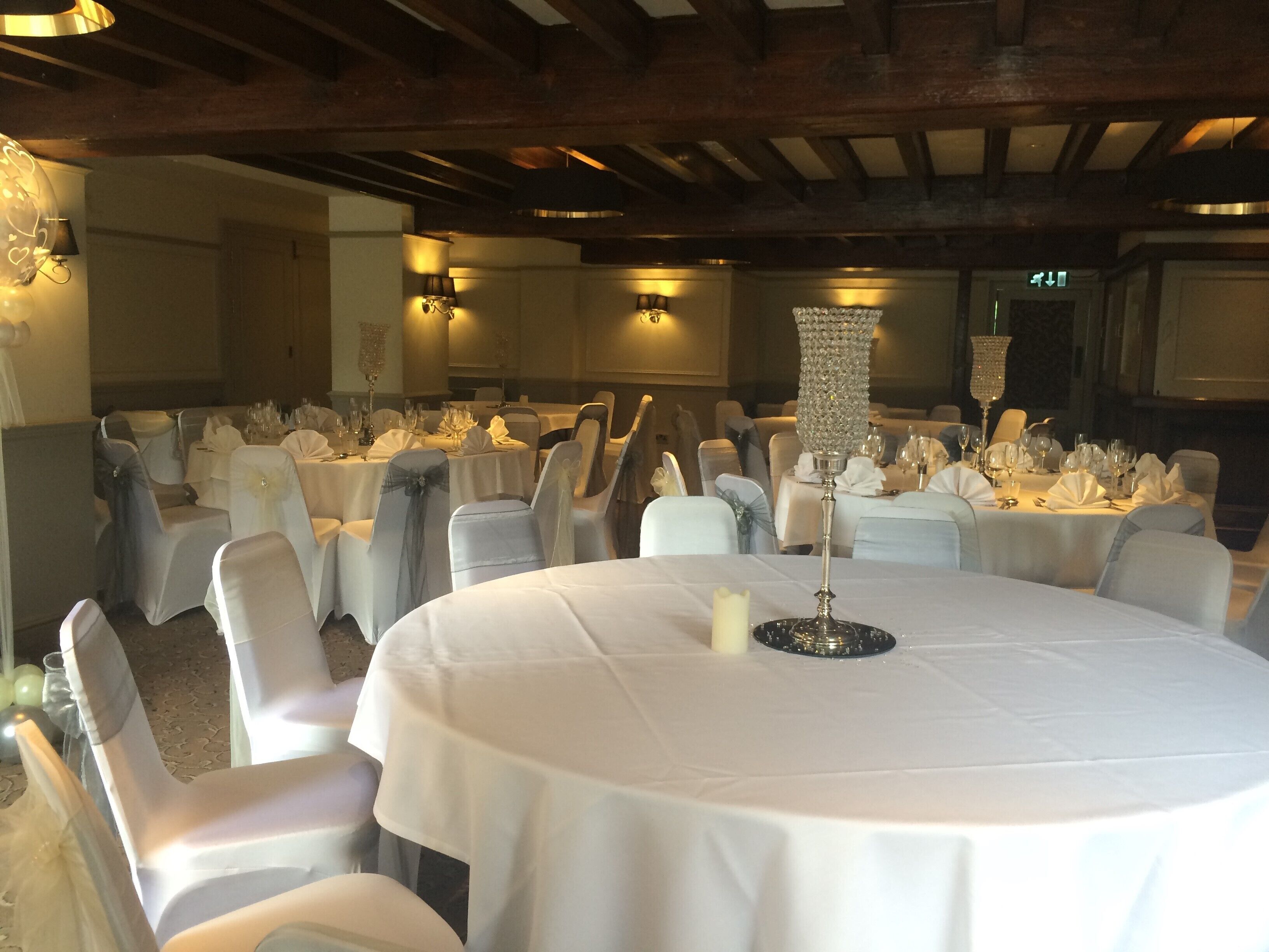 A banquet hall with round tables set for a formal event, featuring white tablecloths, chairs with sashes, and candle centerpieces.