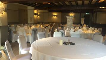 A banquet hall with round tables set for a formal event, featuring white tablecloths, chairs with sashes, and candle centerpieces.