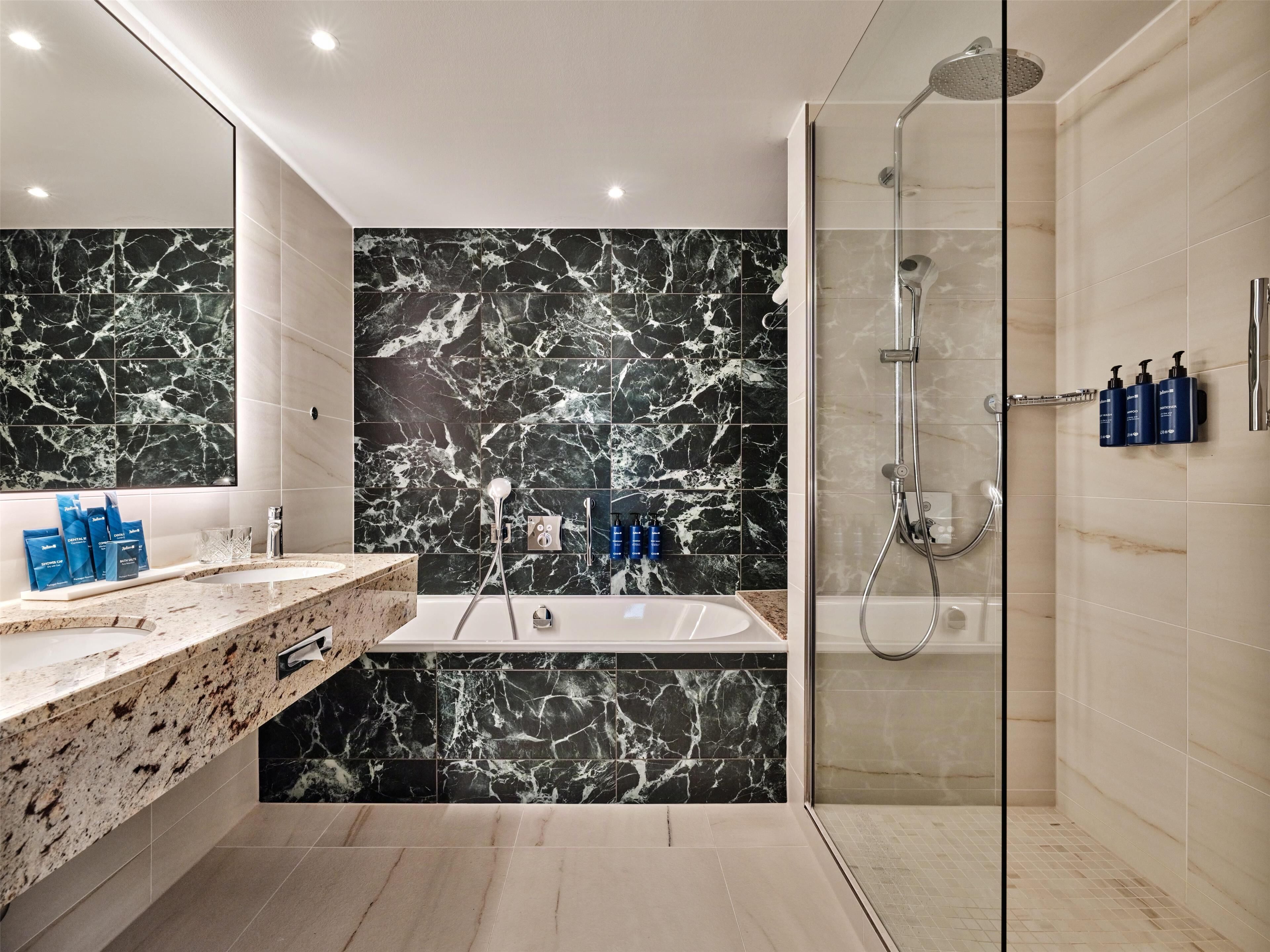 A modern bathroom with a marble vanity, a bathtub, and a glass-enclosed shower area.