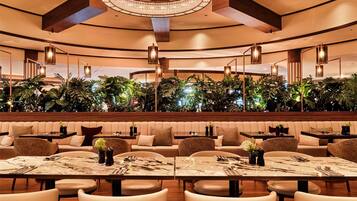 Um restaurante moderno com mesas redondas, assentos acolchoados e um teto com vigas aparentes e um lustre central.