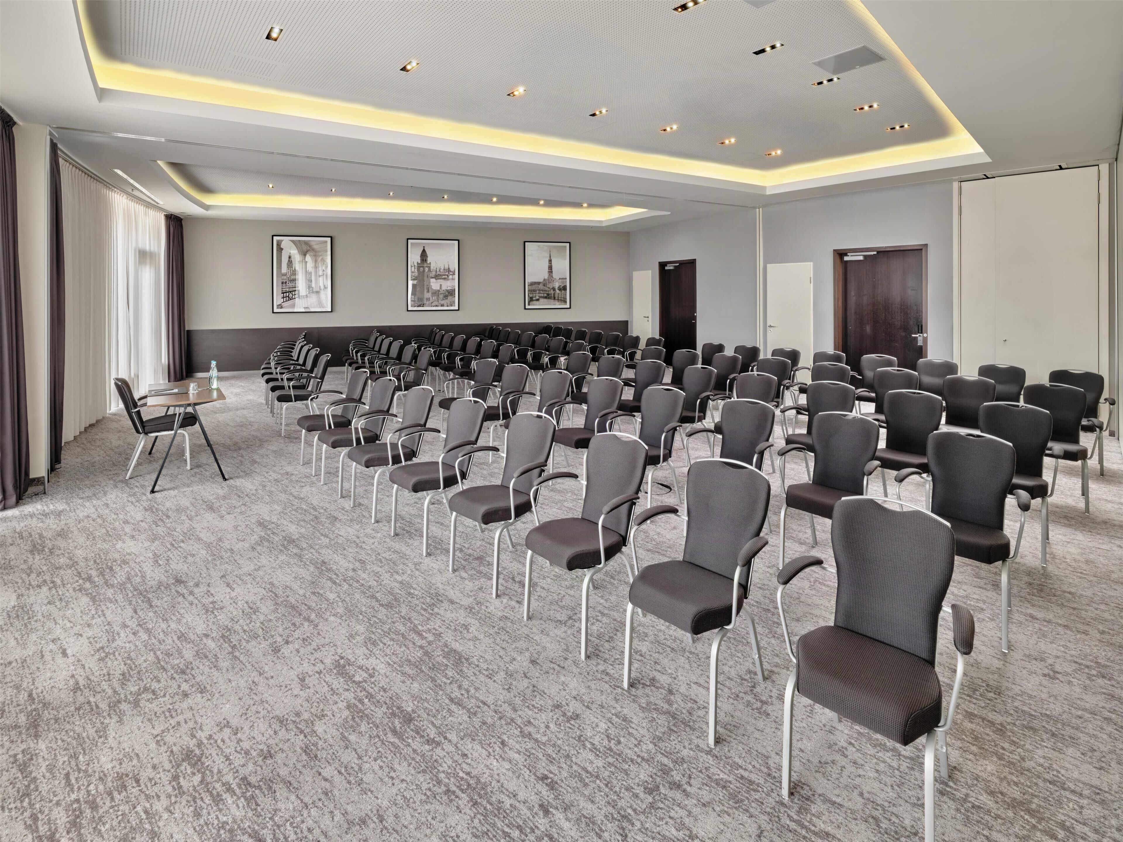 A conference room with rows of chairs, a carpeted floor, and framed pictures on the walls.