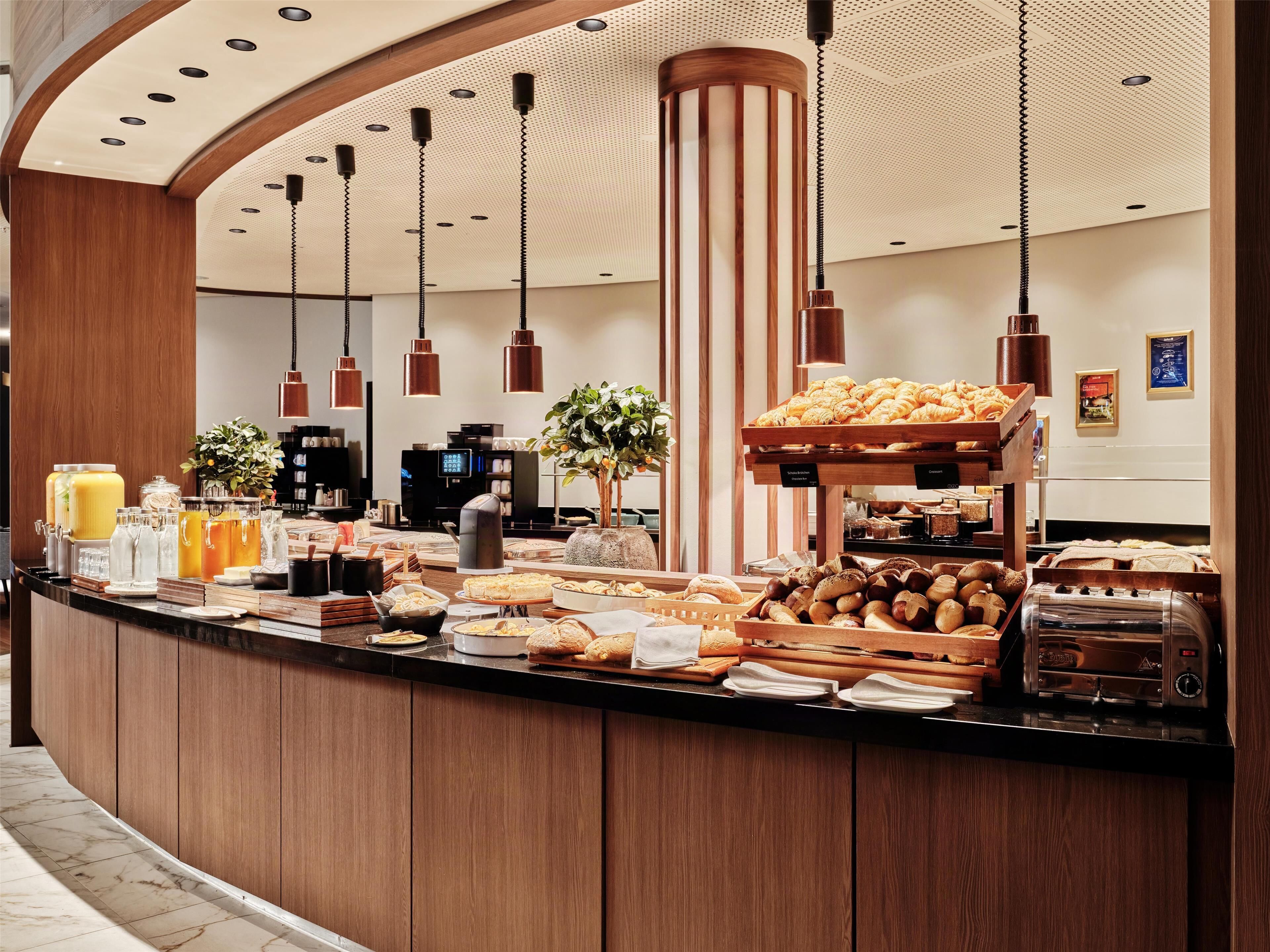 En morgenmadsbuffet med forskellige spisemuligheder, en kaffemaskine og hængende pendellamper.