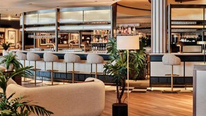 A modern bar area with high stools, a central plant, and a bar counter stocked with bottles and glasses. - Radisson Blu Hotel, Hamburg Airport (Hamburg)