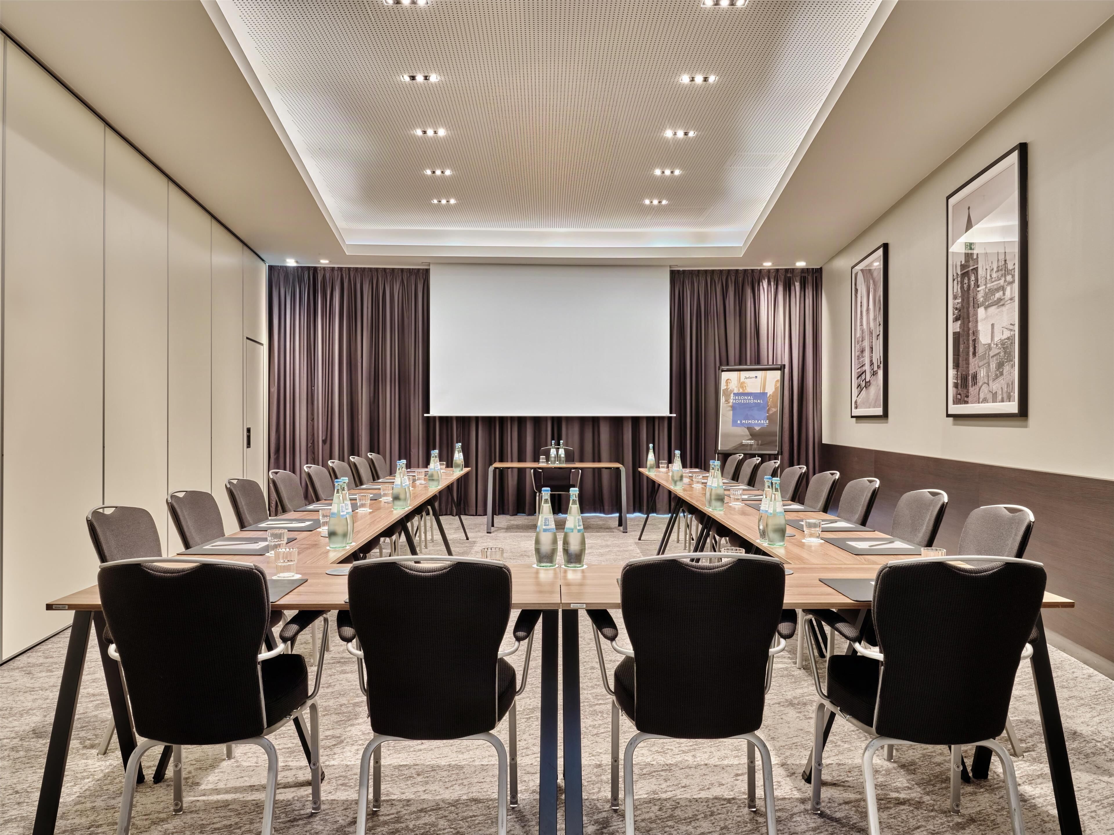 A conference room with a long table, chairs, a projector screen, and a presentation board.