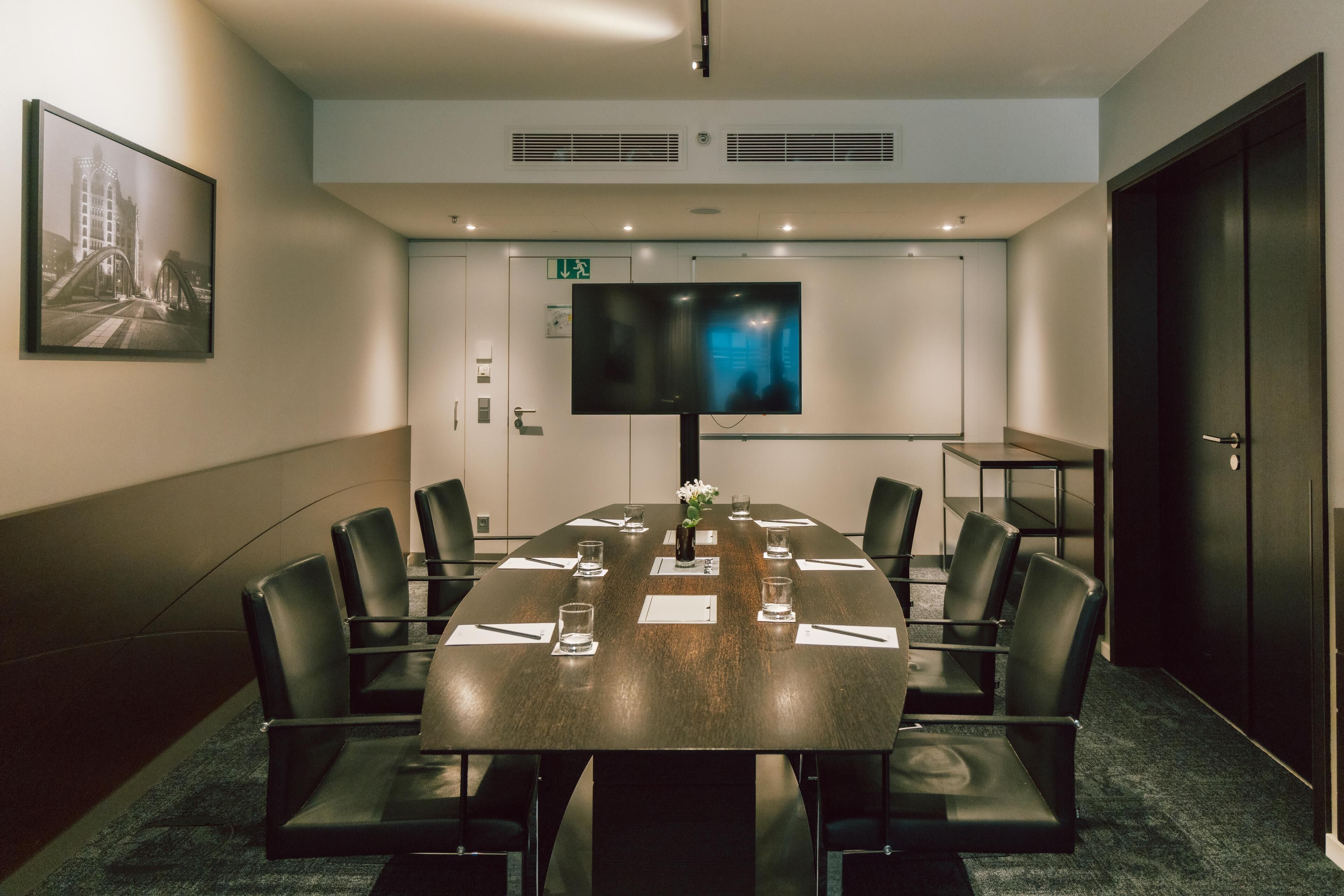 A conference room with a large table, chairs, a TV screen, and a framed picture on the wall.