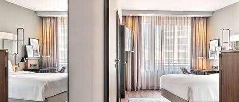 Habitación de hotel con dos camas, un escritorio, una silla, un televisor y una ventana con cortinas.