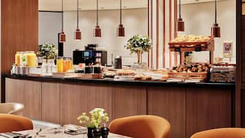 Ein Frühstücksbuffet mit Kaffeemaschine, Obstauslage und einer Auswahl an Gebäck.