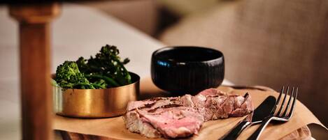 A wooden cutting board with a piece of steak and a bowl of broccoli.