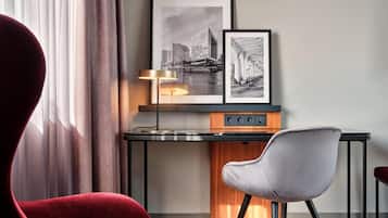 A modern hotel room with a desk, a red chair, and two framed black and white photographs on the wall.