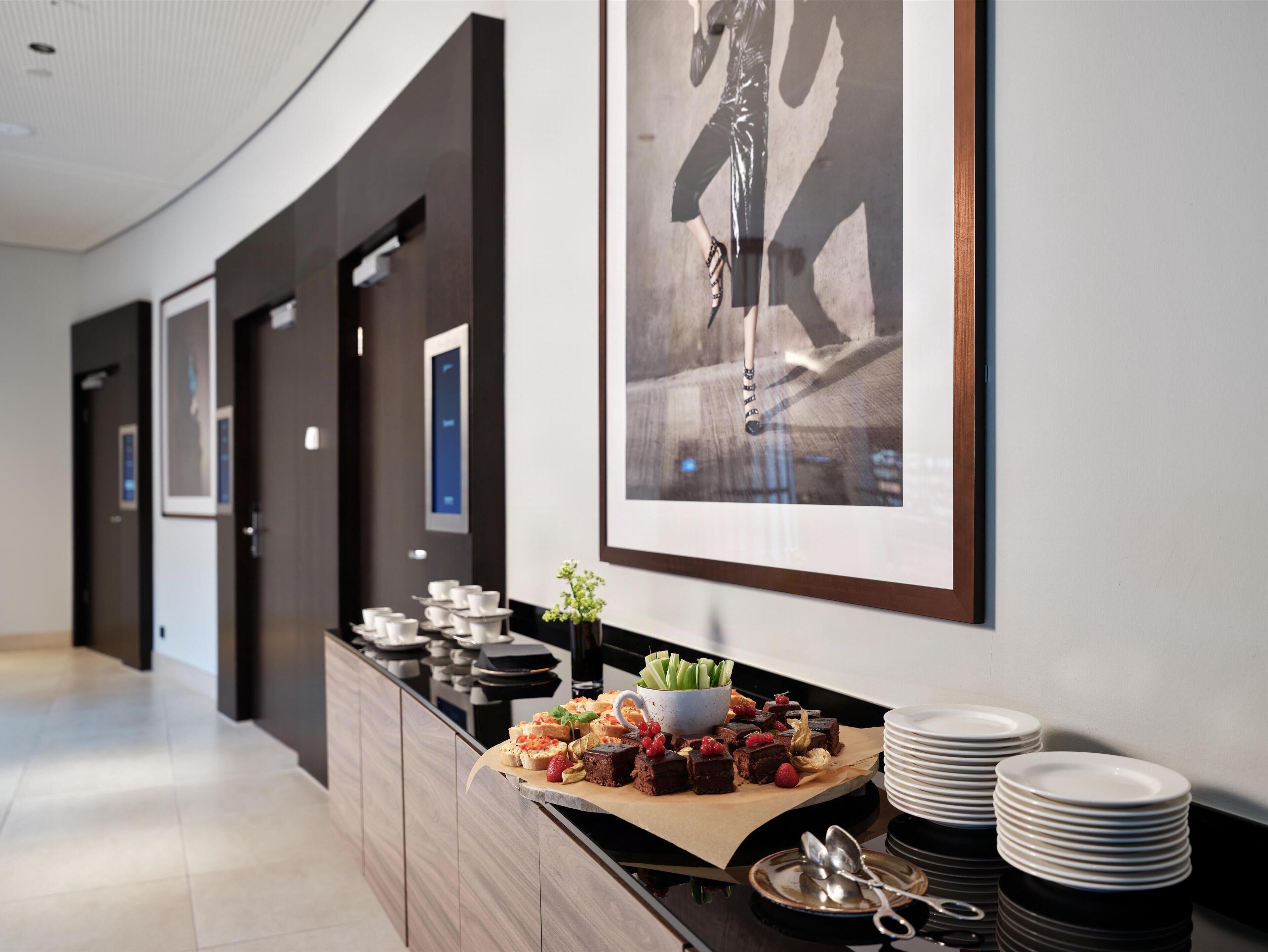 Un pasillo moderno de hotel con una mesa de buffet que presenta diversos postres y un bol de apio.
