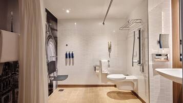 Une salle de bain moderne avec des toilettes, un lavabo et un espace douche. On y trouve trois bouteilles de savon accrochées au mur, un porte-serviettes et un miroir.