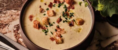 A bowl of creamy soup garnished with croutons and chives, placed on a marble surface with a spoon beside it.