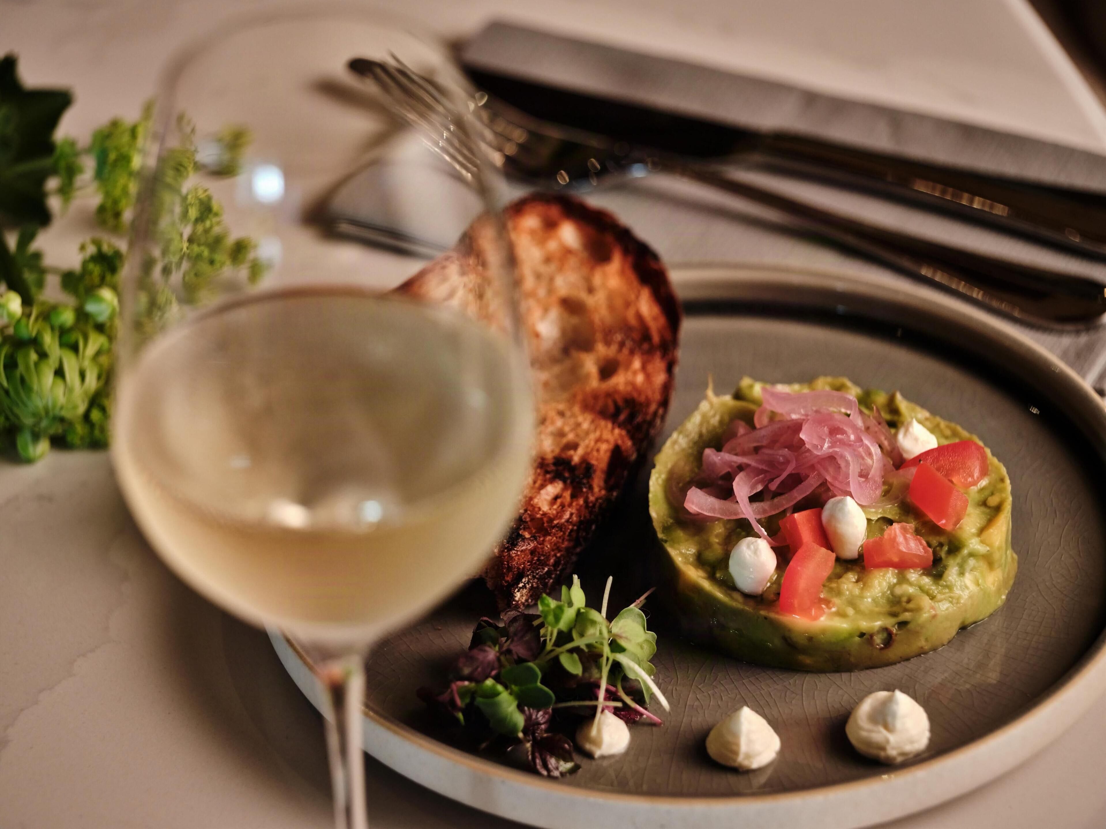 Ein Teller mit Avocado-Salat, ein Glas Weißwein und eine Scheibe Toastbrot.