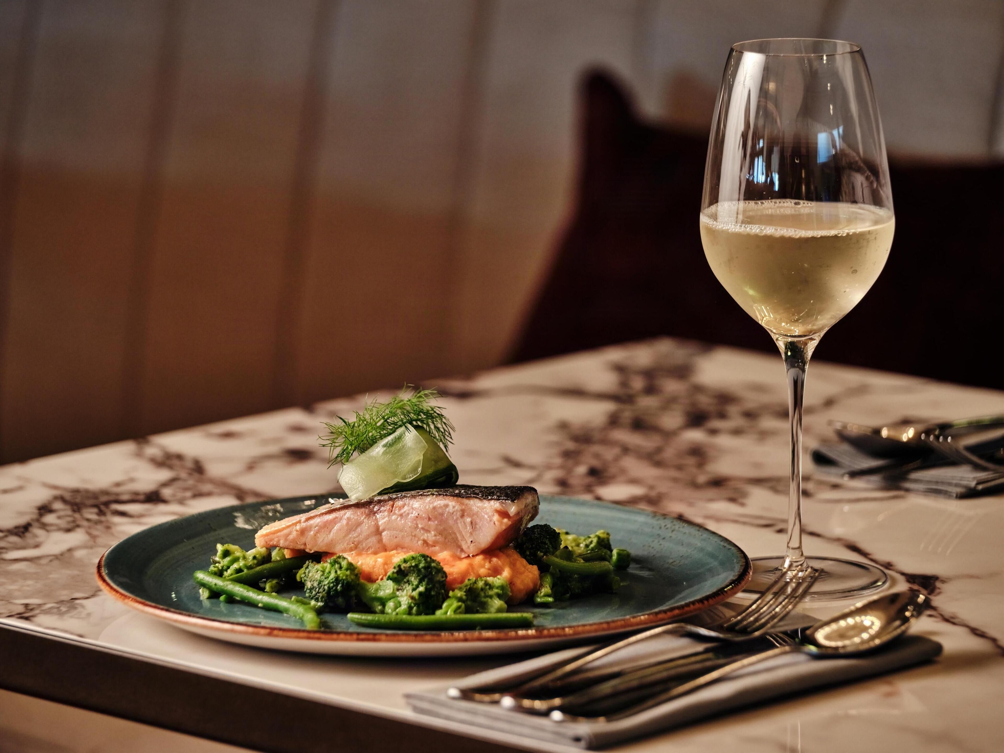 Un plato de comida con una copa de vino blanco sobre una mesa.