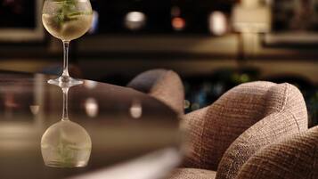 A bar area with a glass of a clear beverage, a cushioned chair, and a reflective surface.