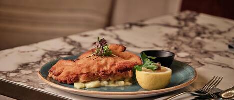 Un plato de pescado frito con una rodaja de limón y decoración sobre una mesa de mármol.
