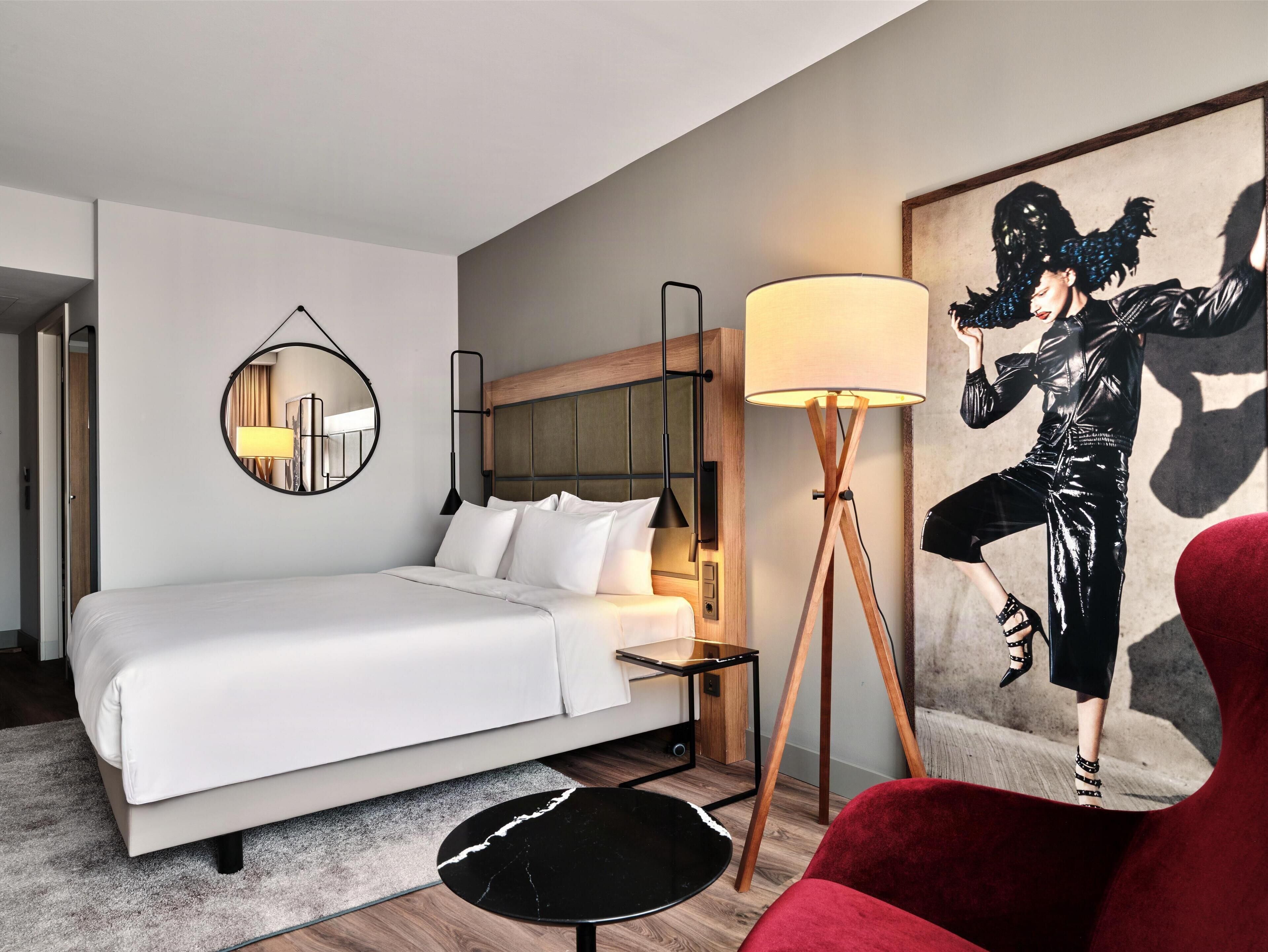 Ein modernes Hotelzimmer mit einem großen Bett, einem Nachttisch, einer Stehlampe und einem roten Sessel.
