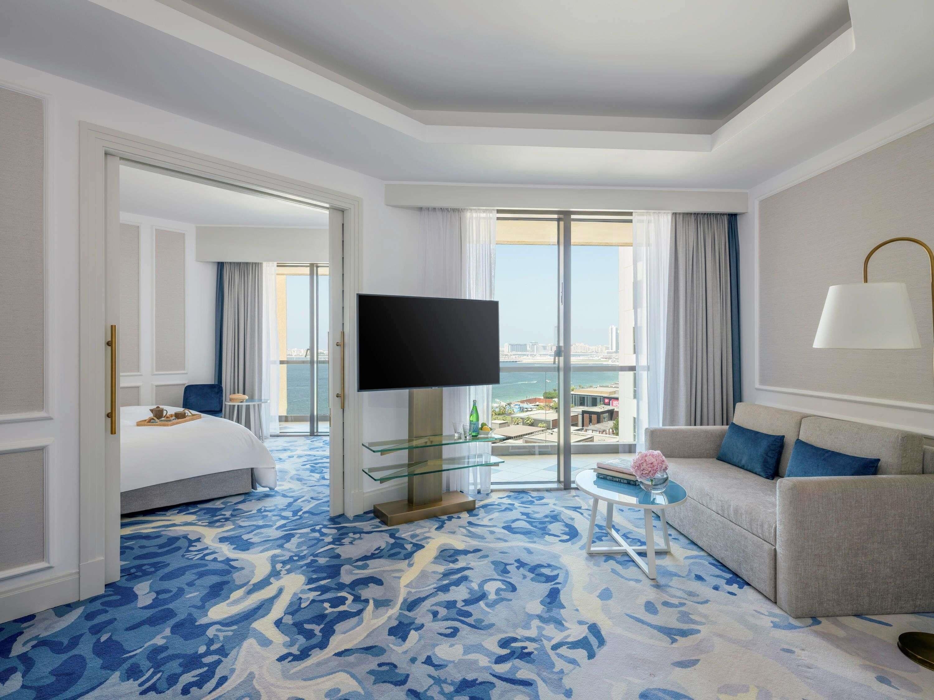 Ein Hotelzimmer mit Bett, Fernseher, Sofa, einem Glastisch und Blick auf die Stadt.