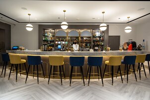 A bar area with a marble countertop, bar stools, and overhead lighting.