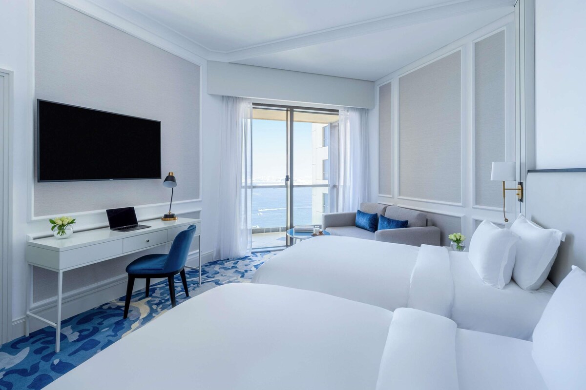 Ein Hotelzimmer mit Bett, Schreibtisch, Stuhl, Fernseher und Meerblick.