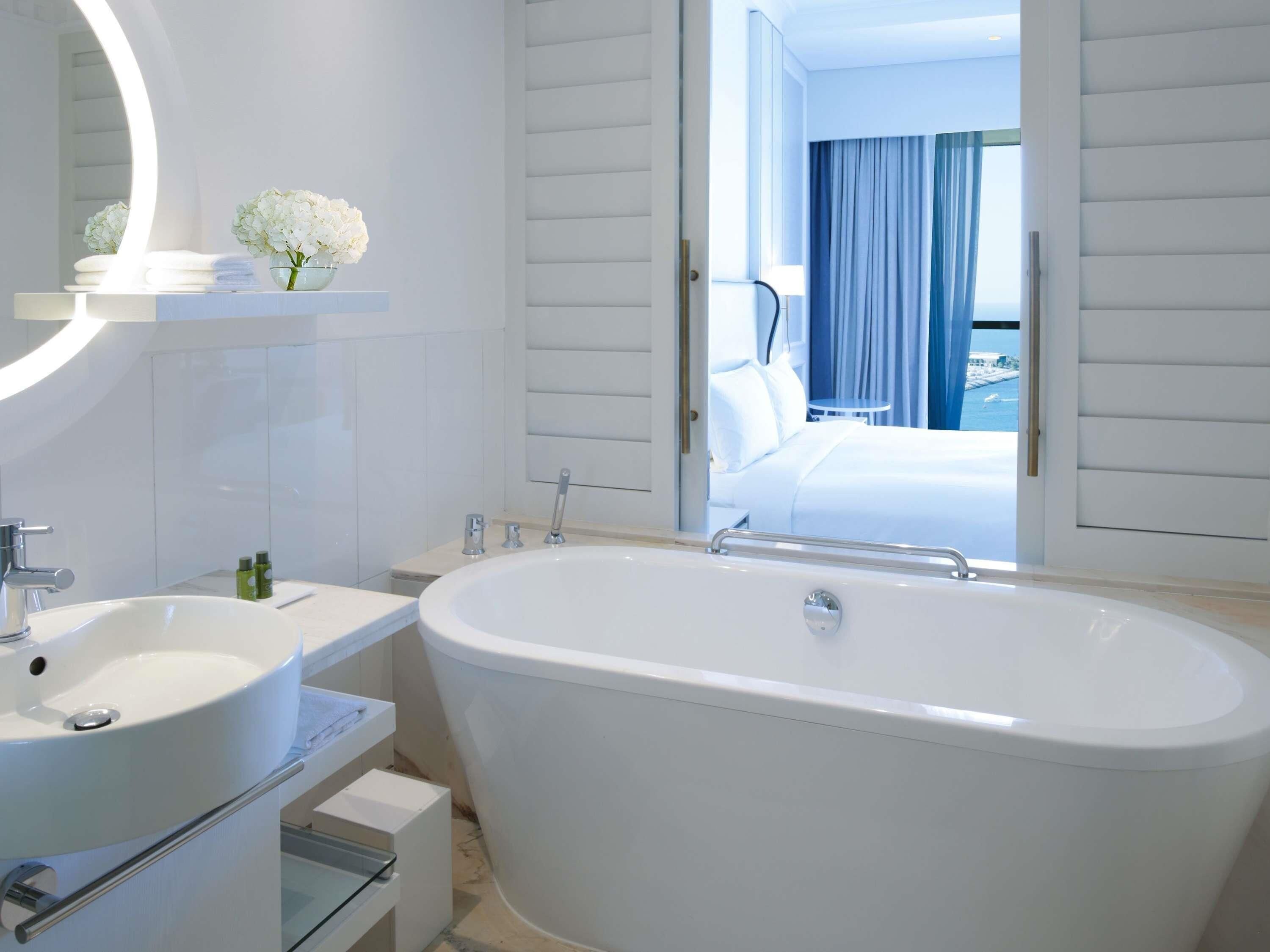 Un baño moderno con una bañera grande, un espejo redondo y un lavabo.