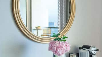 A bathroom with a round mirror, a vase with pink flowers, and a coffee machine.