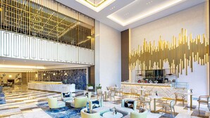 Een ruime lobby met een hoge plafond, een receptiebalie, een zithoek en een decoratieve wand.