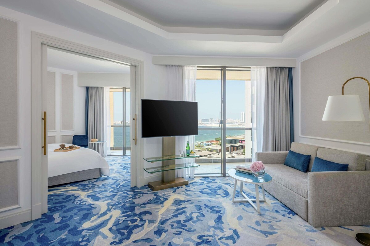Ein Hotelzimmer mit Bett, Fernseher, Sofa, einem Glastisch und Blick auf die Stadt.