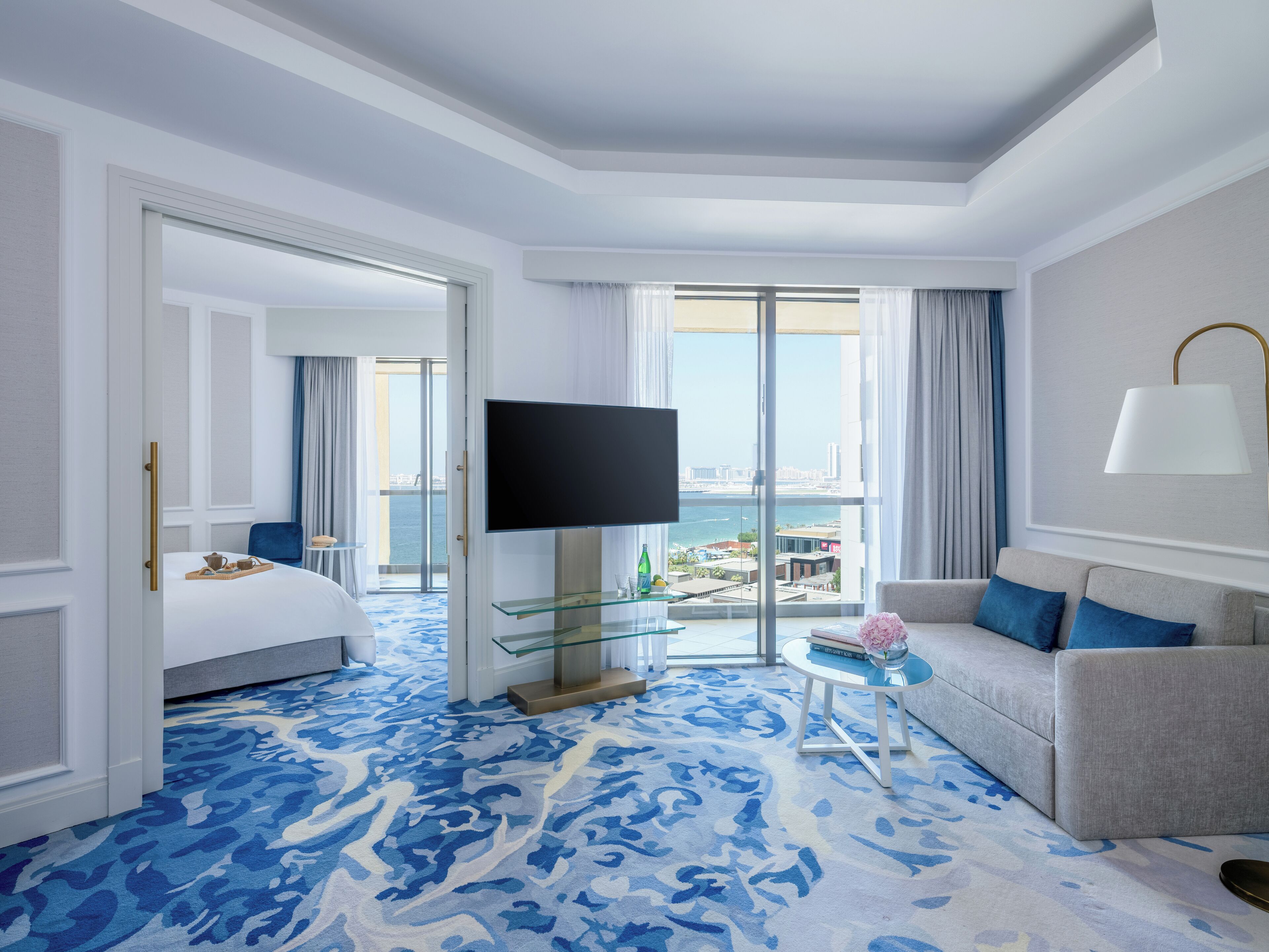 Ein Hotelzimmer mit Bett, Fernseher, Sofa, Glastisch und Blick auf die Stadt.