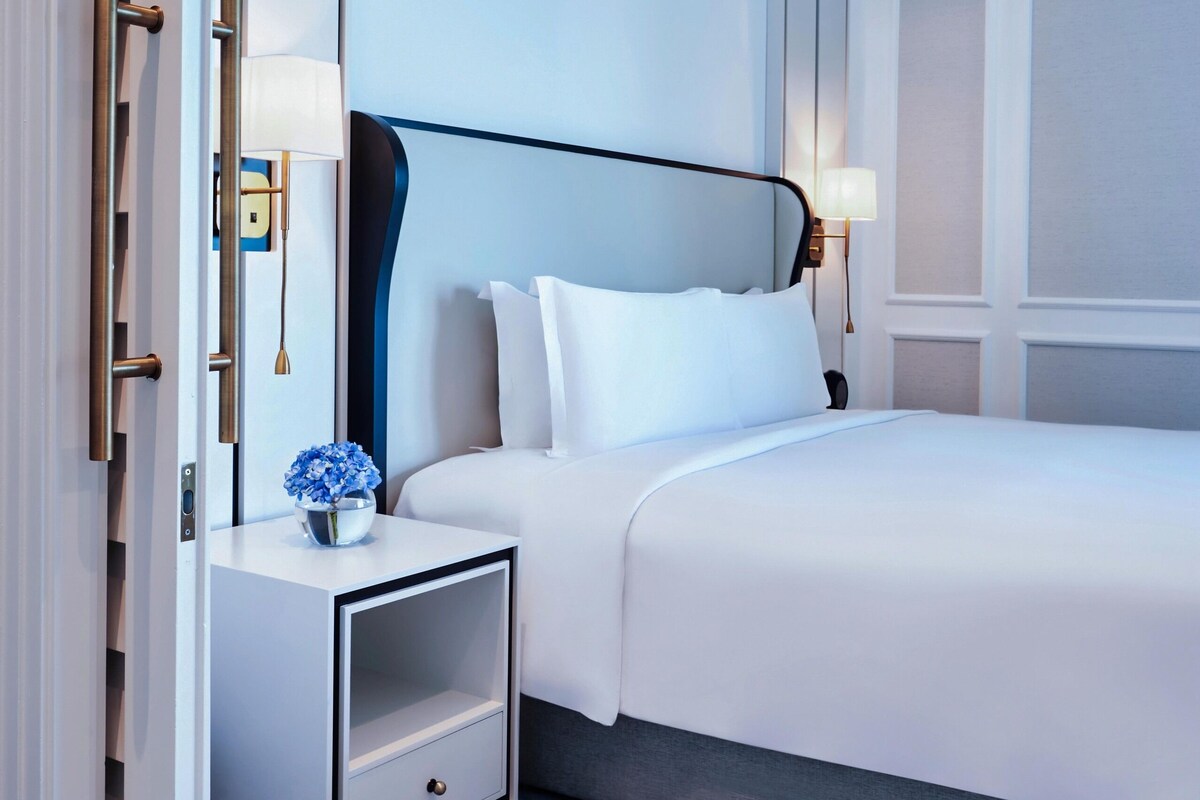 Ein Hotelzimmer mit Bett, Nachttisch, Lampe und einer dekorativen Vase.