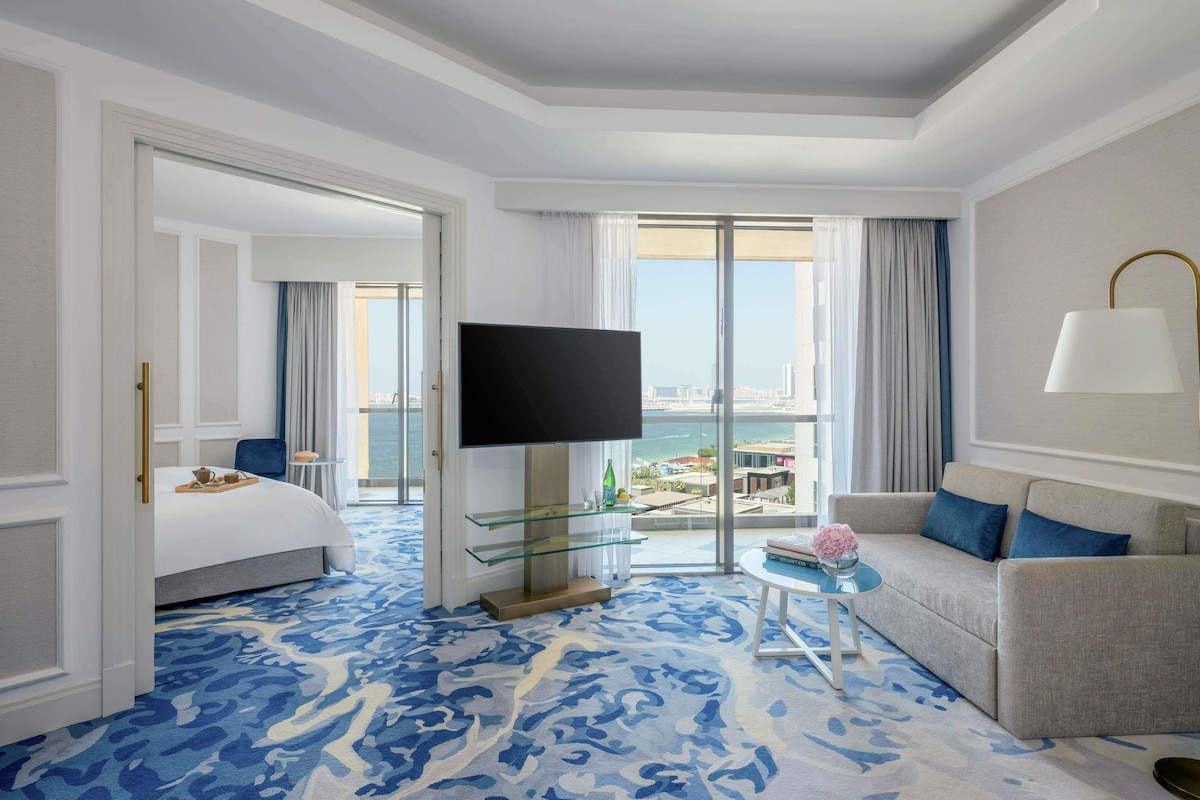 Une chambre d’hôtel avec un lit, une télévision, un canapé, une table basse en verre et une vue sur la ville.