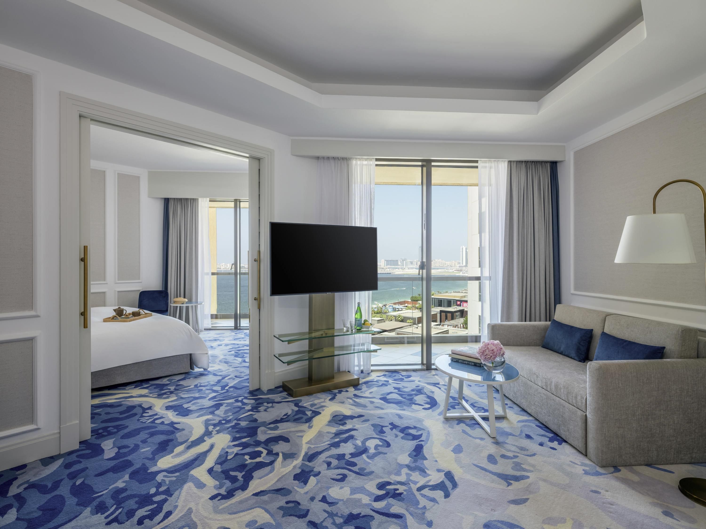 A hotel room with a bed, a TV, a sofa, a small table, and a view of the city.