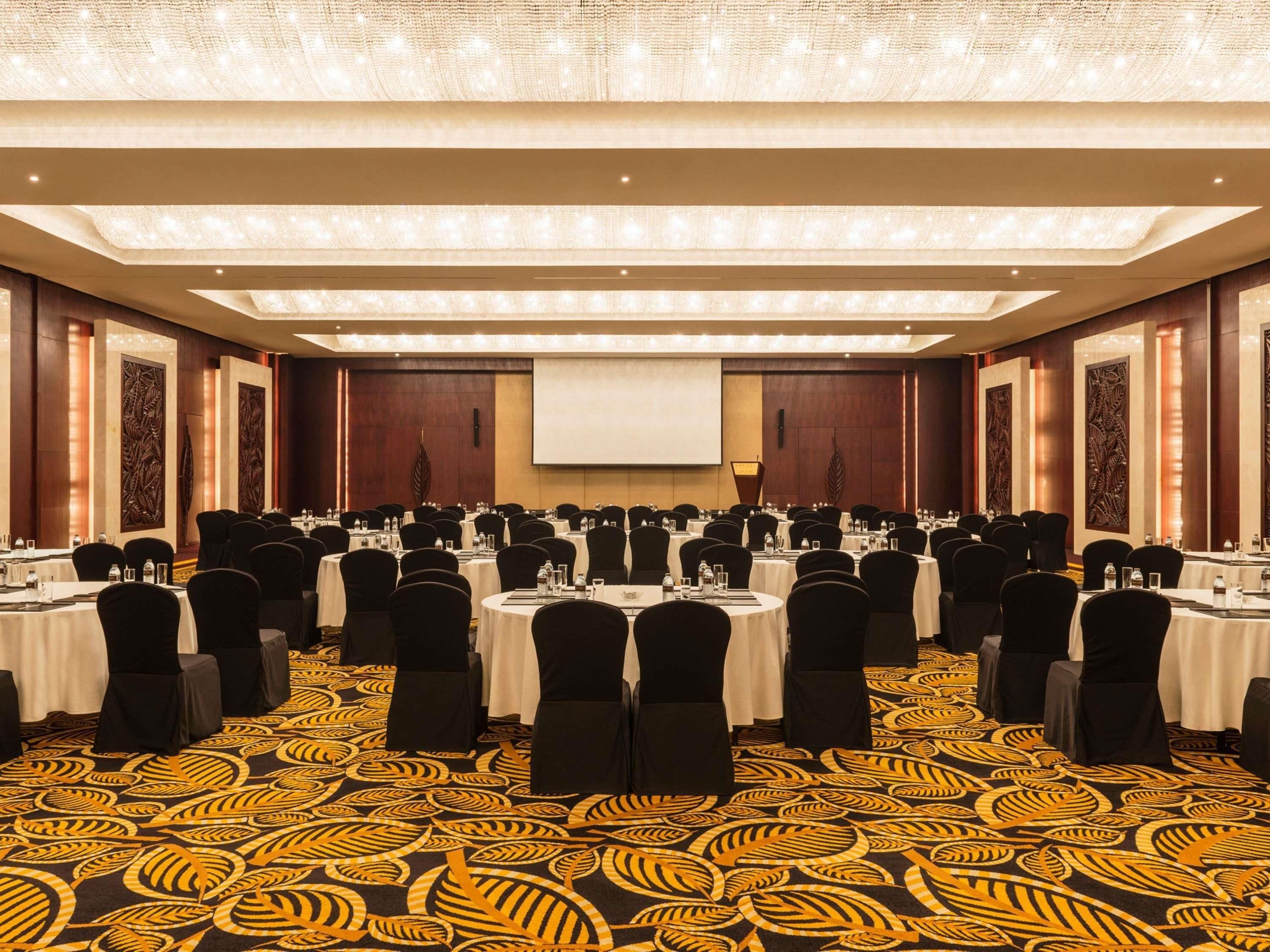 A conference room with round tables, black chairs, and a large screen at the front.