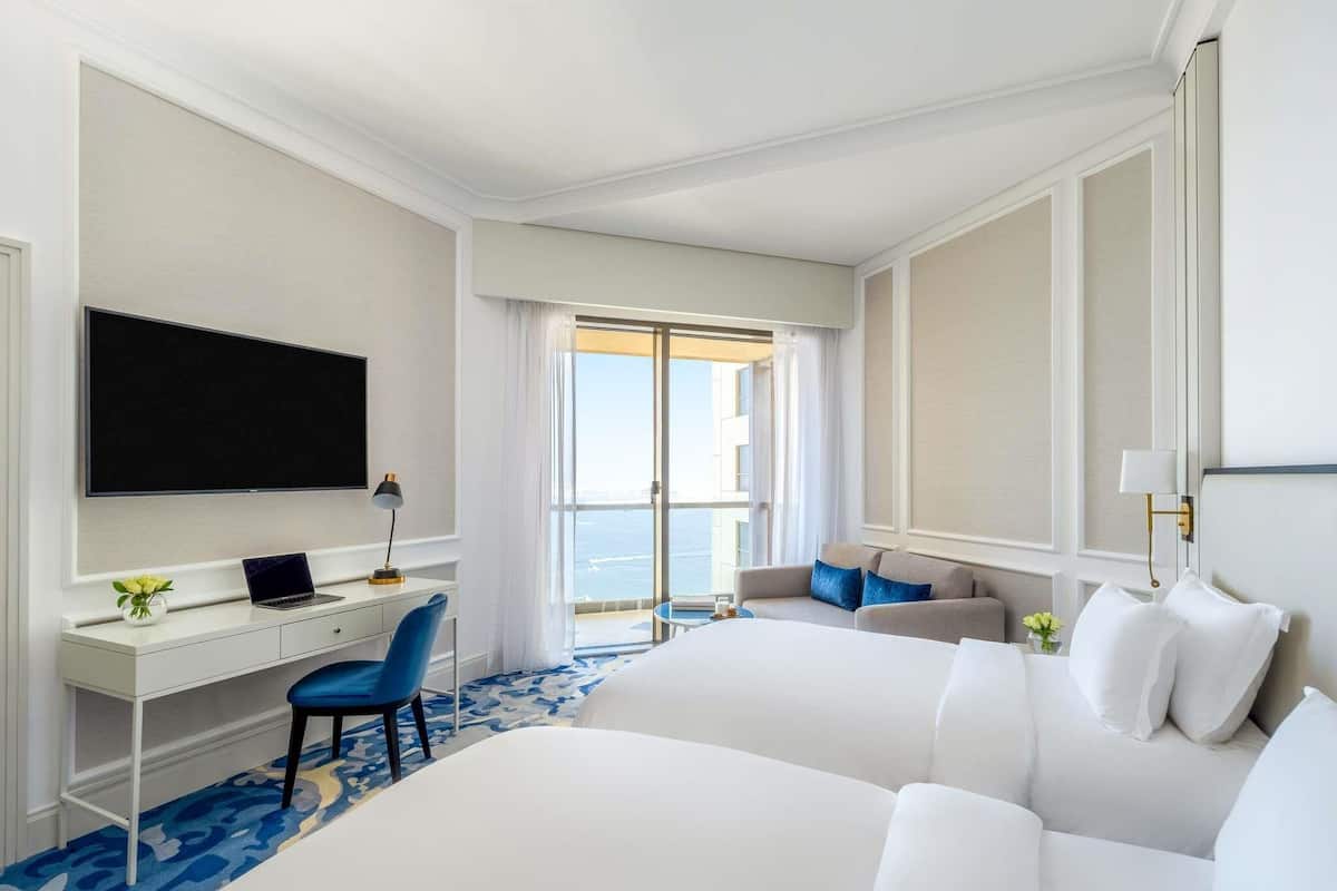 Une chambre dâhĂŽtel avec un lit, un bureau avec un ordinateur portable, une chaise, une tĂ©lĂ©vision et une vue sur lâocĂ©an.