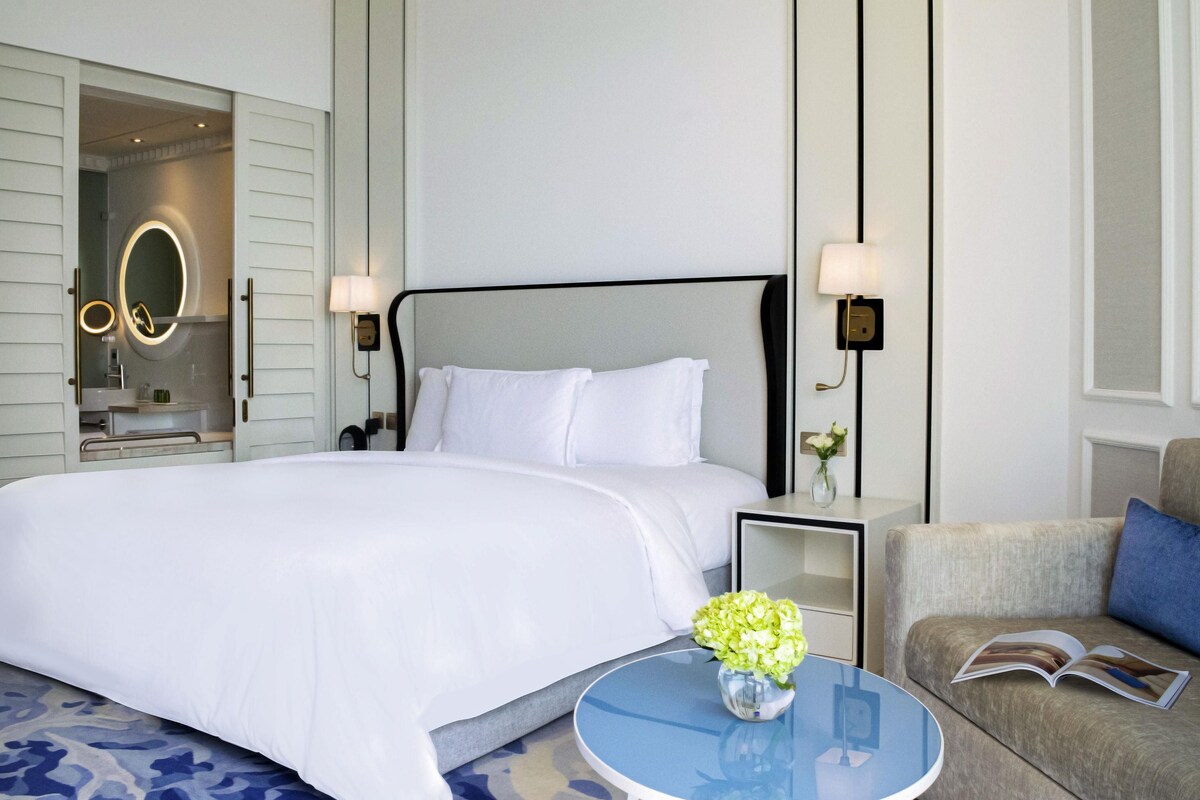Ein Hotelzimmer mit Bett, Nachttisch, Lampe und einem kleinen runden Tisch mit einer Vase.