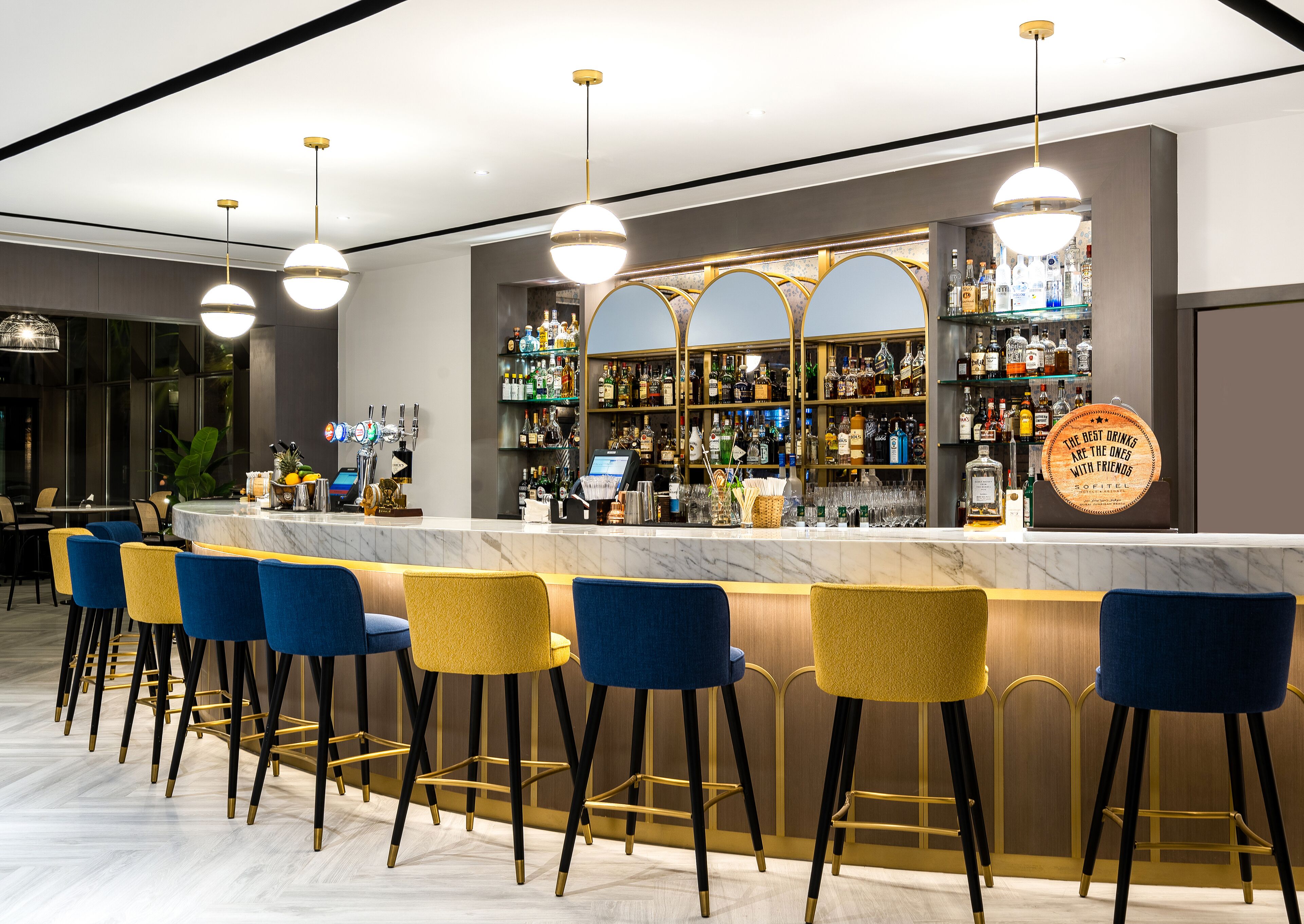 Zona de bar con encimera de mármol, varios taburetes y una variedad de botellas de licor.
