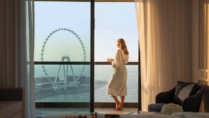 Ein Zimmer mit großem Fenster mit Blick auf ein Riesenrad und eine Brücke, ein Bett mit Frühstücksangebot und ein Sofa.