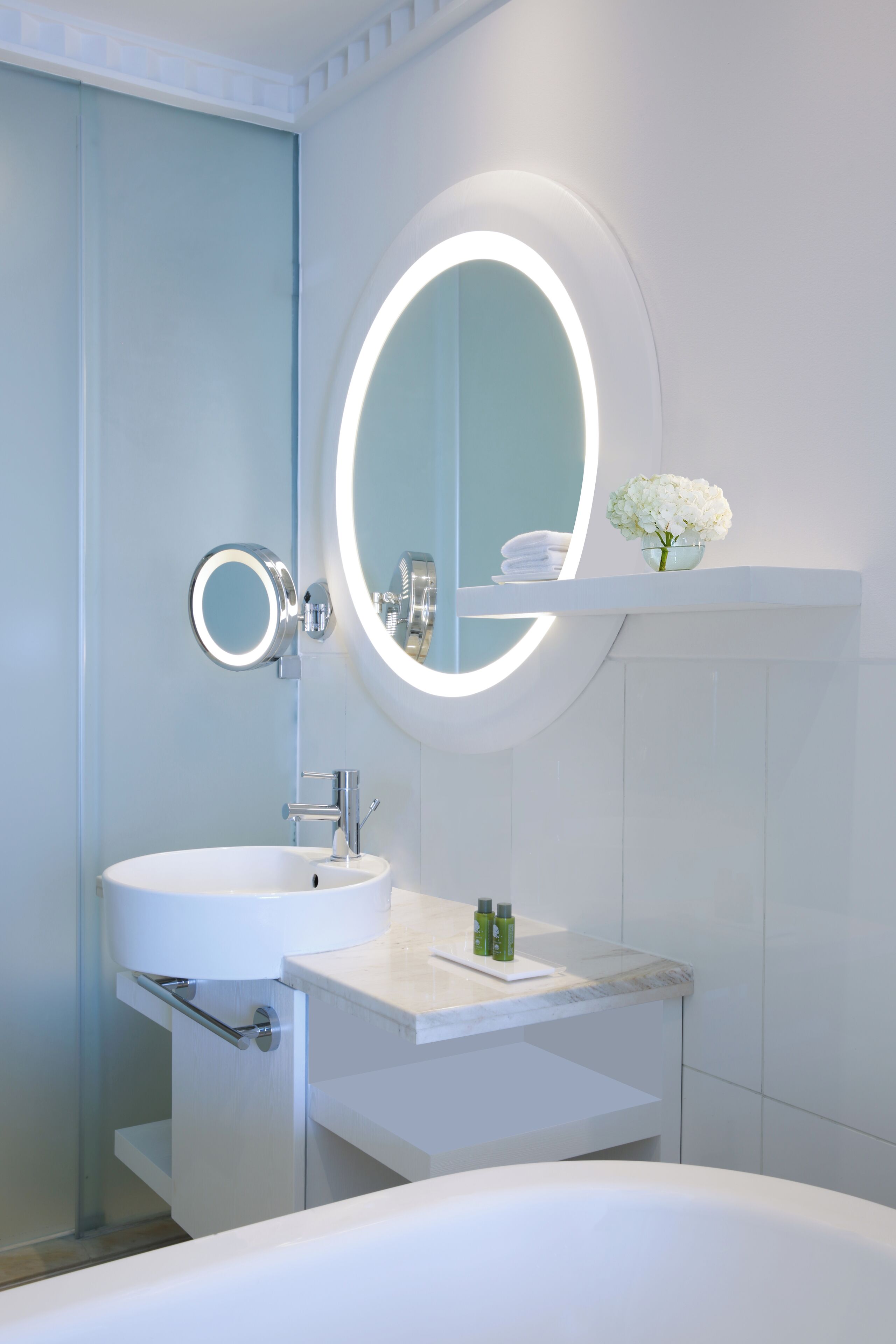 Een moderne badkamer met een witte wastafel, een ronde spiegel met verlichting, en een witte badkuip.
