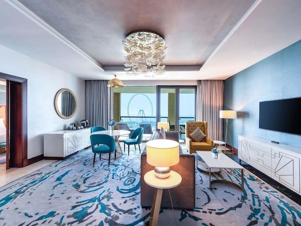 A hotel room with a large window, a chandelier, a TV, and a seating area with a coffee table and chairs.