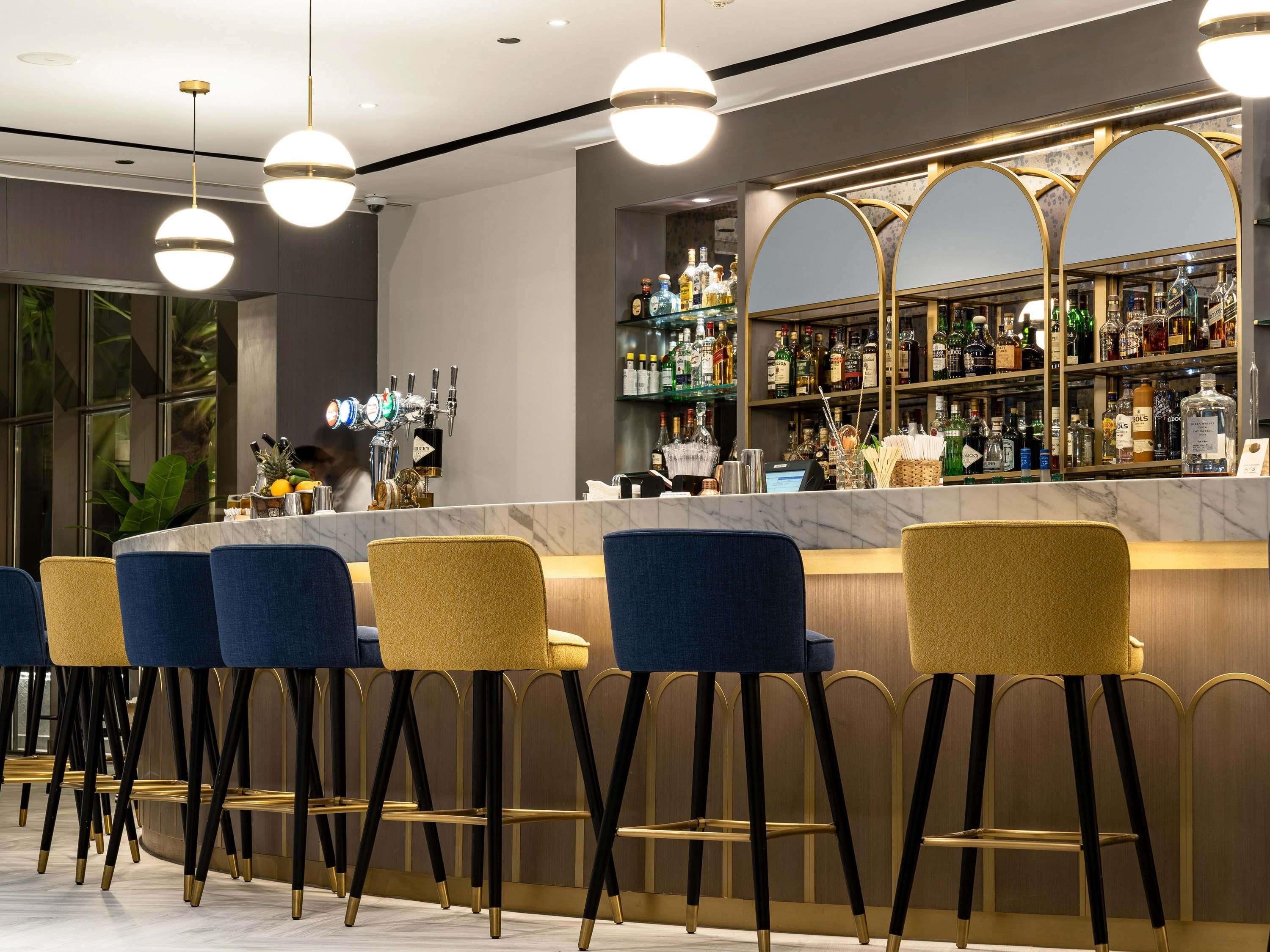A bar area with a marble countertop, multiple bar stools, and a variety of liquor bottles.