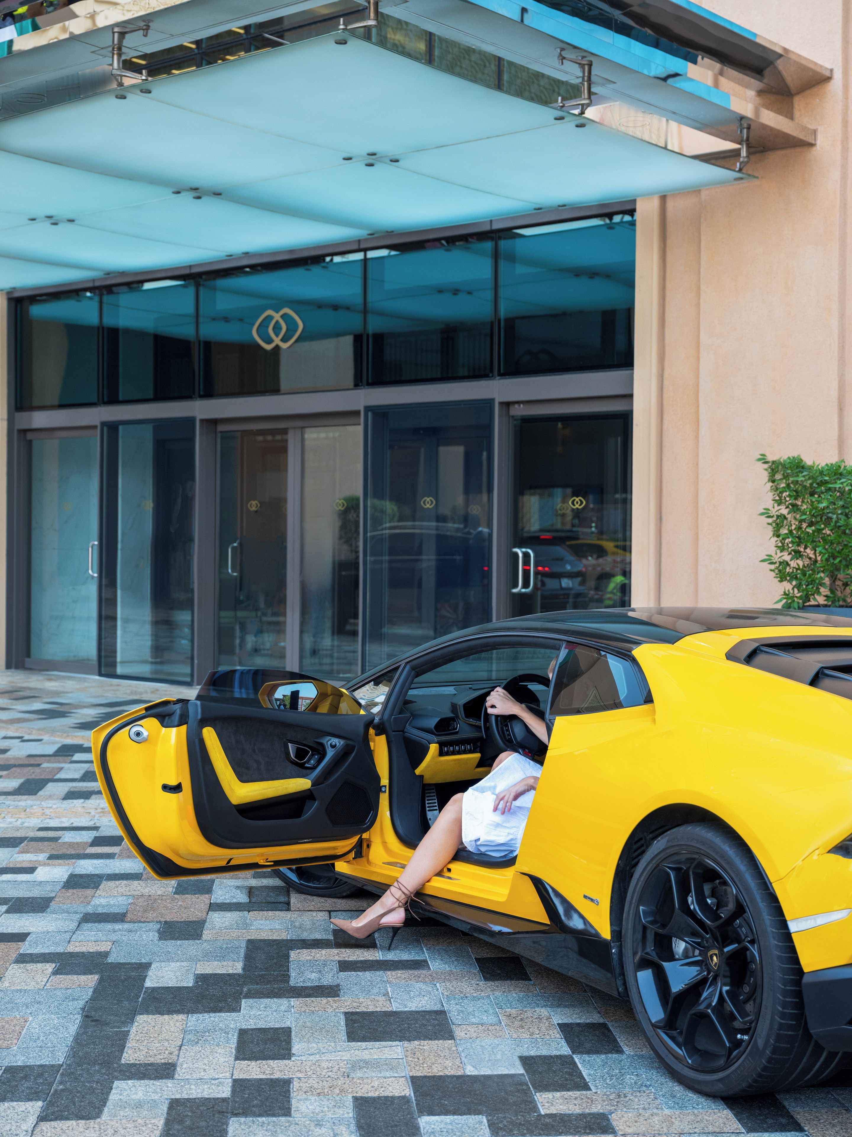 A yellow sports car parked in front of a building with a glass entrance.