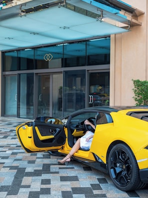 A yellow sports car parked in front of a building with a glass entrance.