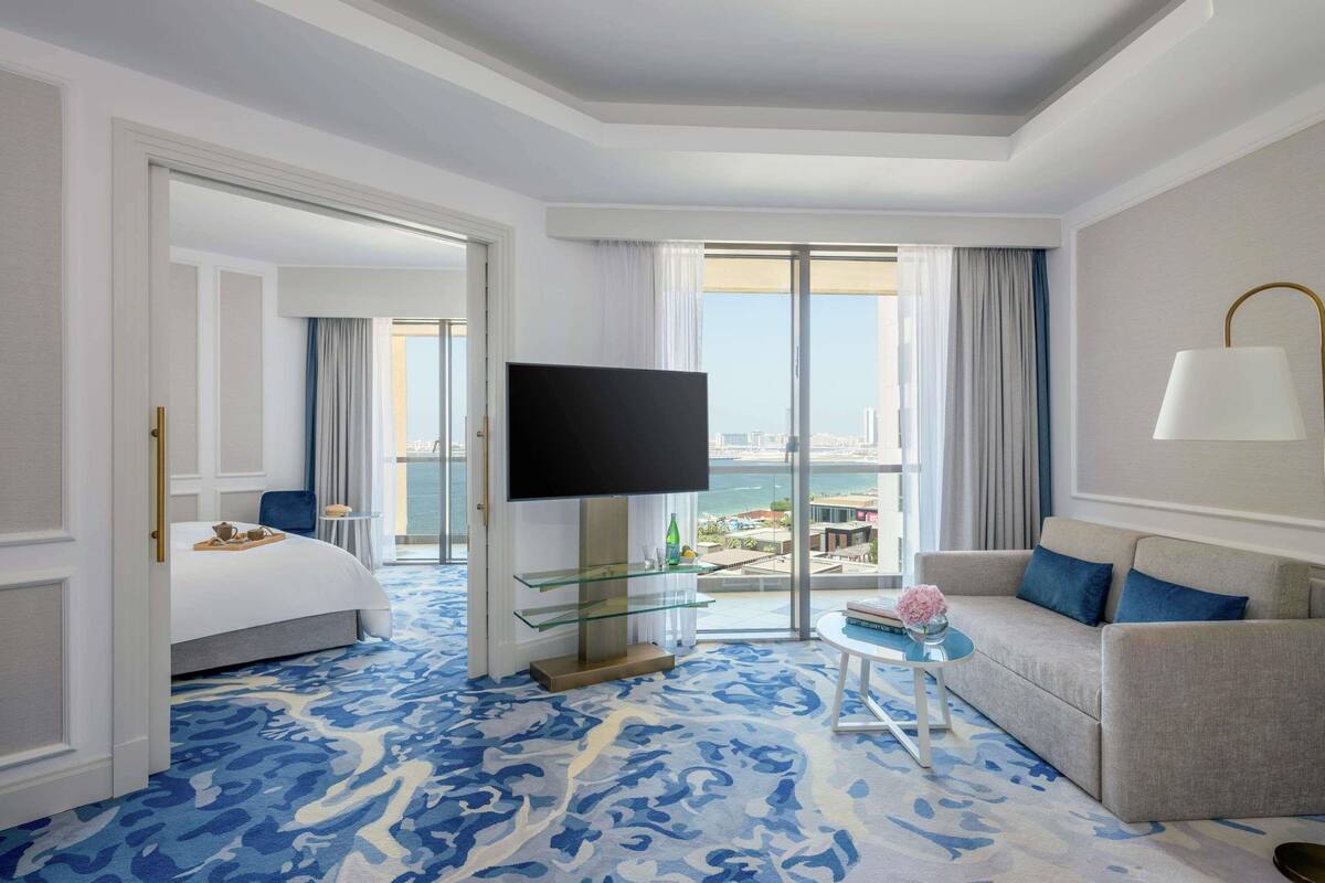 Ein Hotelzimmer mit Bett, Fernseher, Sofa, einem Glastisch und Blick auf die Stadt.
