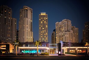 Een hotel met meerdere hoge gebouwen op de achtergrond, een goed verlichte ingang en terrassen.
