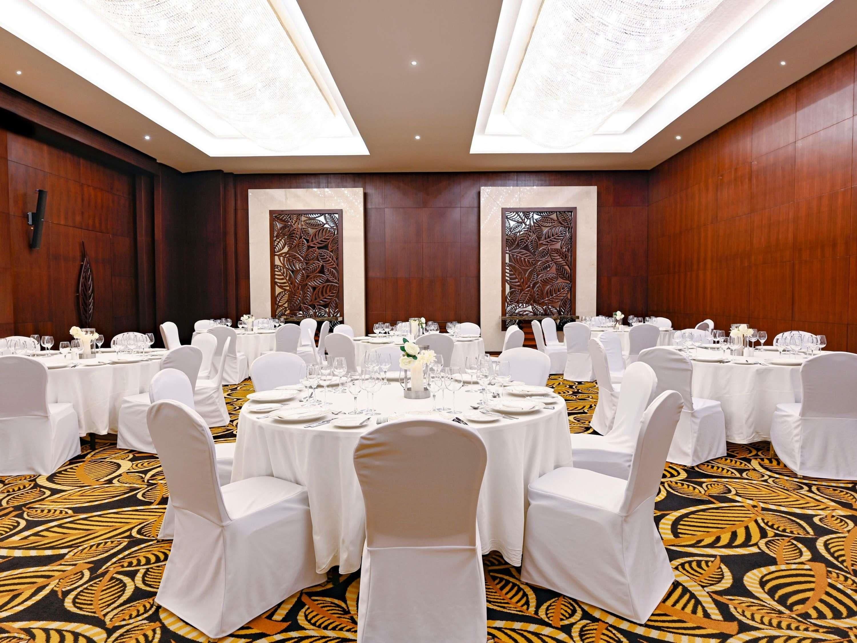A banquet hall with round tables, white chairs, and a patterned carpet.