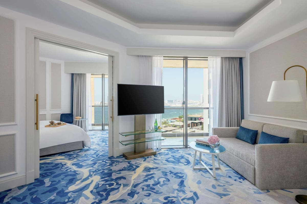 A hotel room with a bed, a TV, a sofa, a glass coffee table, and a view of the city.