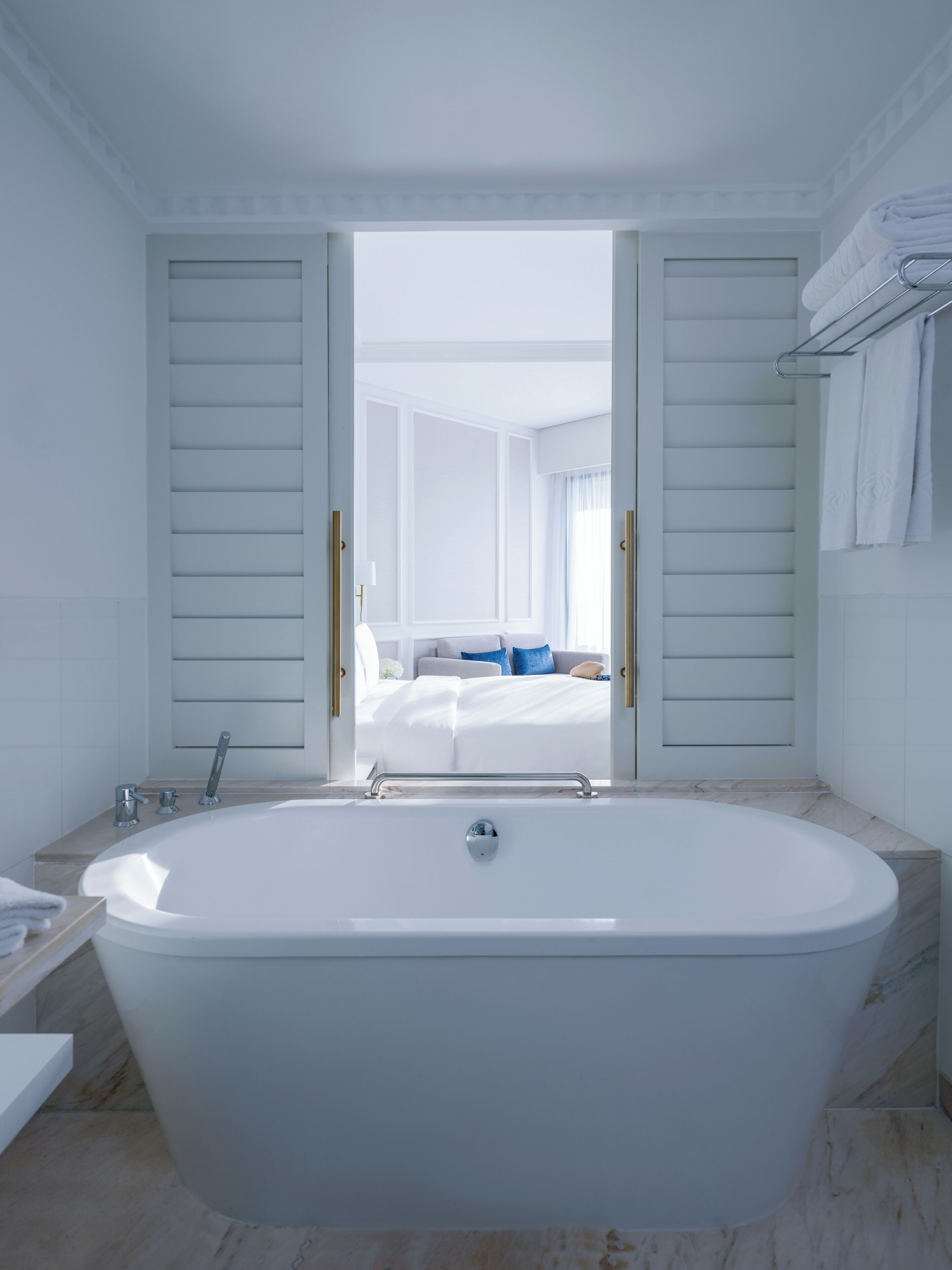 Un baño moderno con una bañera independiente, un tocador con espejo y vistas a un dormitorio con cama y ventana.